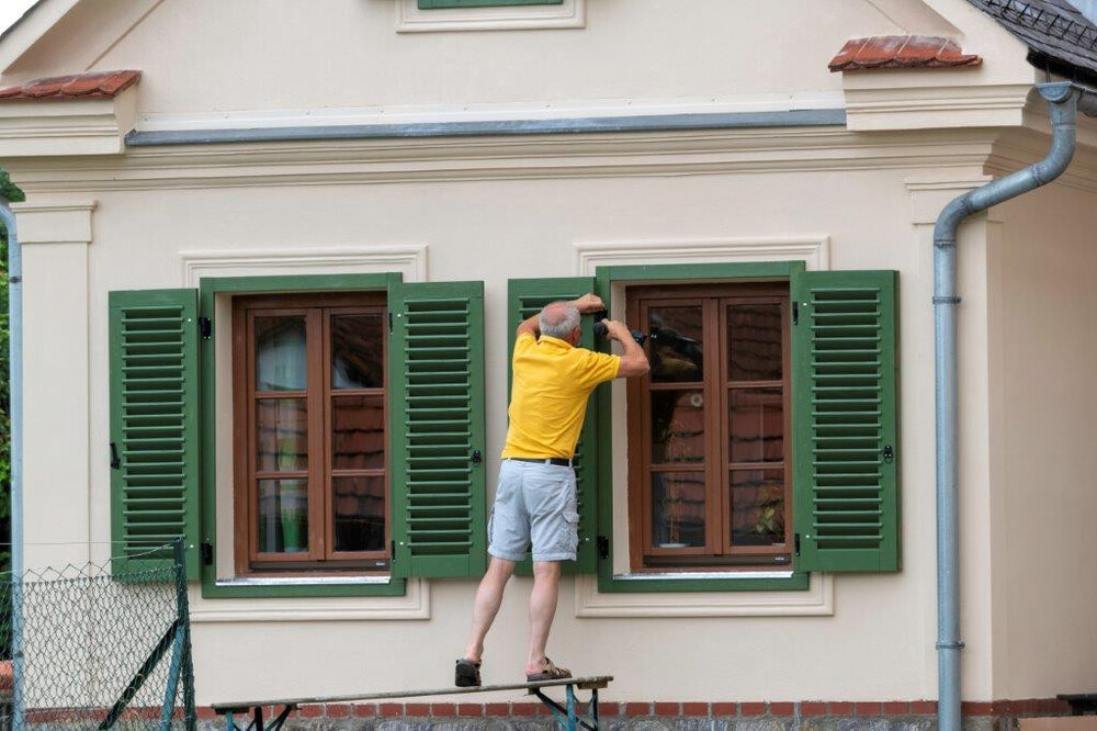 Mann steht auf Gerüst und handiert an einem Fensterladen