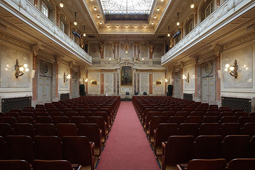 Großer Festsaal in brauner Kinobestuhlung und Galerien an der Seite oben. Vorne die Marmorverkleidung mit Bild von Kaiser Franz Josef